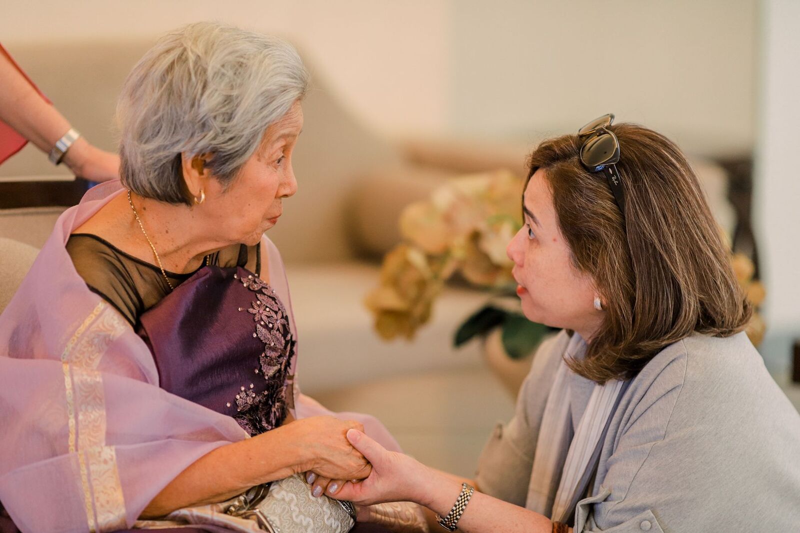 Older woman holding her adult daughter's hands as they talk at home