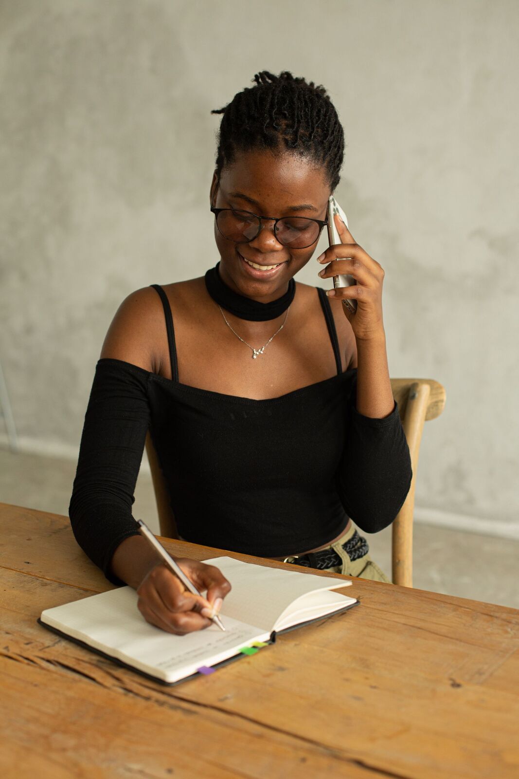 Woman taking notes at a table while talking on the phone